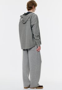 Kariran sivi in črni hoodie s ohlapnimi sivimi trenirkami. Hlače imajo širok kroj, kar dopolnjujejo rjave čevlje.