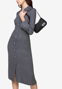 Knapp-up kjole i mørkegrå stof med lange ærmer, sideslids og krave. Sammen med en lille sort håndtaske.