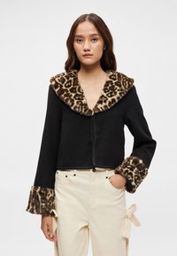 Casaco preto cropped com gola e punhos em pelagem sintética de estampado de leopardo, apresentando um fecho frontal trançado e mangas longas.