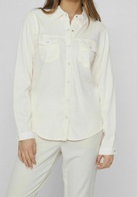 Chemise à manches longues en ivoire, en tissu doux, avec deux poches poitrine à boutons-pression et un col classique.