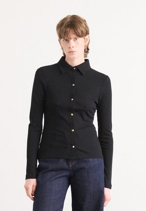 Zwarte langekraagshirt met een kraag, geribbeld textuur en gouden knopen aan de voorkant, gestyled met donkerblauwe jeans.