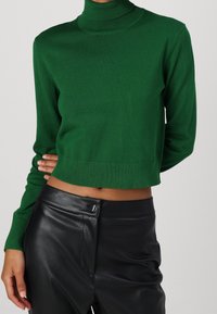 Pull vert court à col roulé en tissu tricoté doux. Il présente des manches longues et un col ainsi qu'un ourlet côtelés pour un ajustement parfait.
