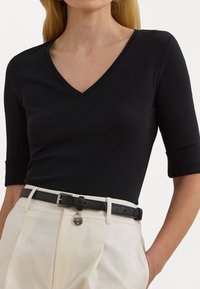 Zwarte V-hals top met driekwartmouwen, gecombineerd met beige high-waisted broeken en een zwarte riem met een zilveren slotdetail.