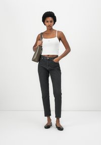 Jeans neri in denim abbinati a una canotta bianca, completati da una borsa verde e scarpe flat nere, su uno sfondo bianco semplice.