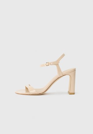 Beige high-heeled sandal with ankle strap and gold buckle, open toe, and block heel on a white background.