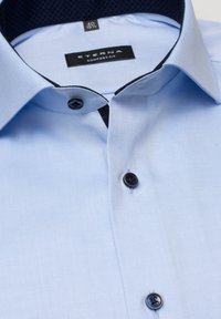 Camicia button-up azzurro chiaro in design comfort fit. Presenta un colletto interno scuro a motivo, due bottoni scuri e una trama del tessuto liscia.