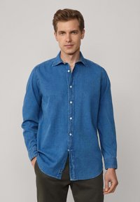 Denim overhemd in medium blauw, met een puntige kraag, een knoopsluiting aan de voorkant, lange mouwen en een ronde zoom met een klein logo-label aan de zijkant.