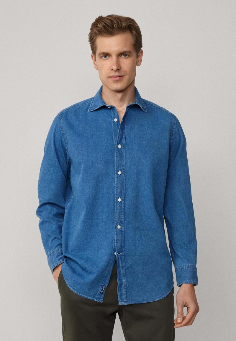 Denim overhemd in medium blauw, met een puntige kraag, een knoopsluiting aan de voorkant, lange mouwen en een ronde zoom met een klein logo-label aan de zijkant.