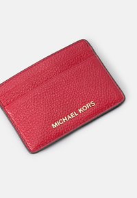 Red leather cardholder with textured finish, featuring multiple card slots and gold embossed branding. Edges are black, adding contrast.
