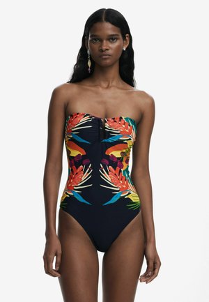 En-delad baddräkt med strapless-design, livlig tropisk tryck i röd, grön och blå på en mörk marin bakgrund.