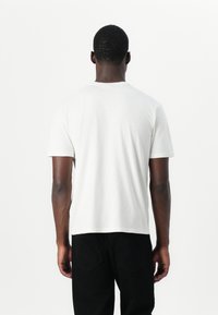 White cotton t-shirt with short sleeves, crew neck, and a relaxed fit. Simplistic design, paired with black trousers. No visible patterns.