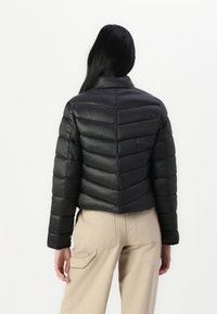 Doudoune noire, design court, motif en chevrons, finition brillante, col montant et manches longues. Associée à un pantalon cargo beige.