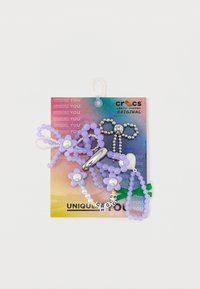 Crocs Jibbitz charms set met paarse en pastel kralen, bloemvormen, een zilveren charm, en een verscheidenheid aan texturen en kleuren op een kaart.