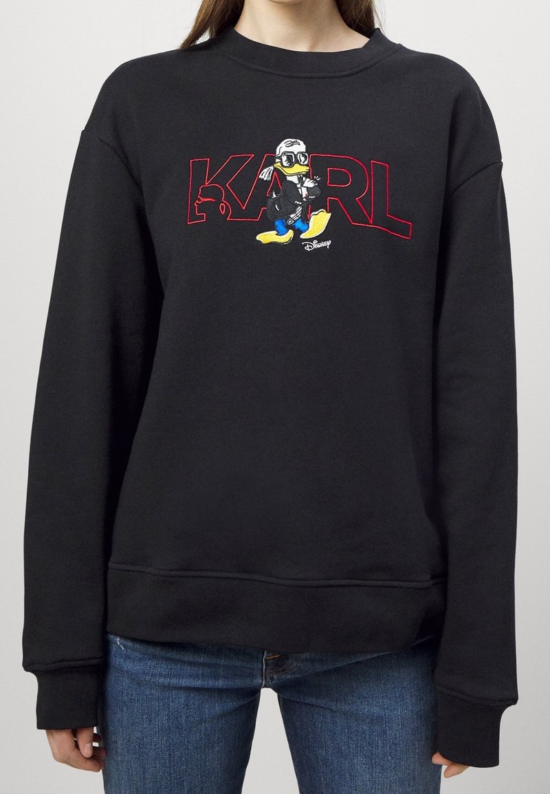 Sweat-shirt noir avec texte contouré en rouge "KARL" et un canard dessin animé portant des lunettes et une veste noire devant le texte.