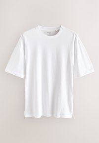 T-shirt blanc uni à manches courtes et col rond suspendu sur un fond beige clair, étiquette taille moyenne.