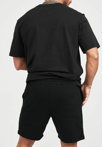 Svart bomulls t-shirt med kort ärm och matchande svarta shorts, med resårmidja och en bakficka med en strukturerad detalj.