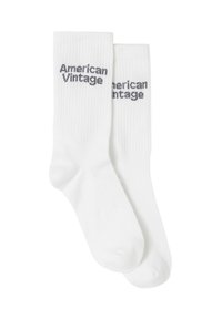 Calcetines de algodón blancos con una textura acanalada y el texto "American Vintage" en gris, impreso en el lado exterior.