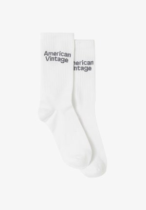 Kerge hall fliisdress, millel on lõdva lõikega, pikad varrukad ja ümar kaelus. Kombineeritud valgete sokkidega, millel on must tekst.