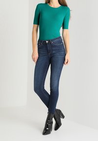 Teal ribbed short-sleeve top paired with dark blue skinny jeans, complemented by black heeled ankle boots with shiny finish.