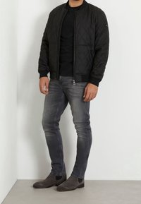 Chaqueta bomber negra acolchada con puños acanalados, combinada con una camiseta negra, jeans ajustados grises y botines de ante grises.