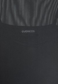 Gros plan sur un tissu noir texturé avec un détail subtil plissé et un petit logo brodé "even&odd" en blanc au centre.