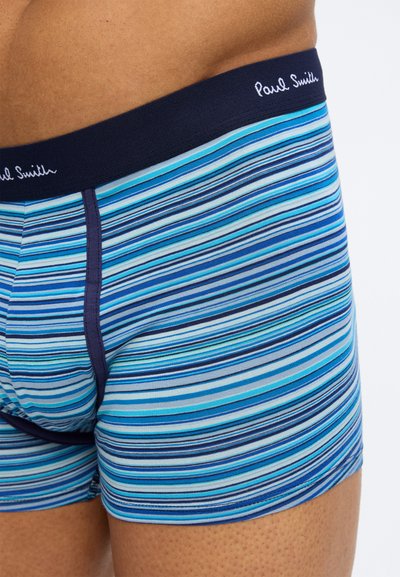 Torso masculin portant un boxer à rayures bleues, turquoise et marine avec le logo "Paul Smith" sur la ceinture.