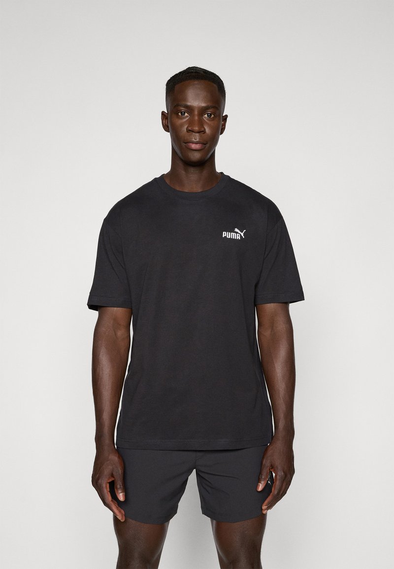 Sort bomulds-t-shirt med korte ærmer, med et hvidt Puma-logo på venstre bryst, parret med sorte shorts. Simple design og tekstur.