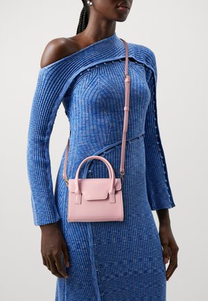 Liten rosa läderhandväska med strukturerad design, övre handtag och justerbar rem, bärs över en ribbad blå klänning.