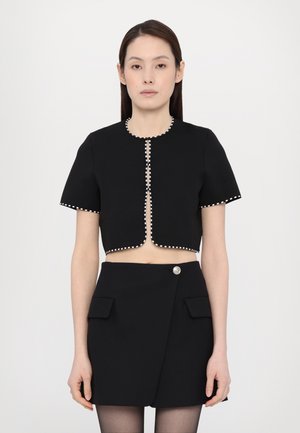 Black cropped jacket with short sleeves, trimmed with white piping, open front. Skirt is black, wrapped style, featuring two front pockets and a button.