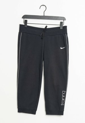 Czarne skrócone spodnie treningowe Nike z białymi paskami po bokach, ściągaczem w pasie i napisem "training" na dolnej części nogawki, wiszące na czarnym wieszaku.