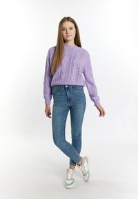 Lila gestrickter Pullover mit Zopfmuster, kombiniert mit hellblauen Skinny-Jeans und mehrfarbigen Sneakers mit weißen und mintgrünen Akzenten.