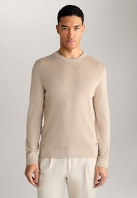 Maglione beige in maglia con scollatura rotonda e maniche e orlo a coste. Presenta una superficie testurizzata e un logo discreto sul lato.