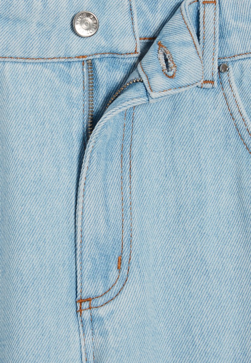 Denim bleu clair avec un bouton en métal visible, une fermeture éclair et des coutures orange contrastantes. Présente une texture légèrement usée et des bords effilochés.