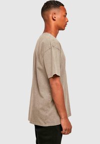 Verblasstes taupefarbenes T-Shirt mit kurzen Ärmeln und Rundhalsausschnitt, das einen entspannten Schnitt und dezente Nähte aufweist. Einfarbige Stoffstruktur, ohne Muster.