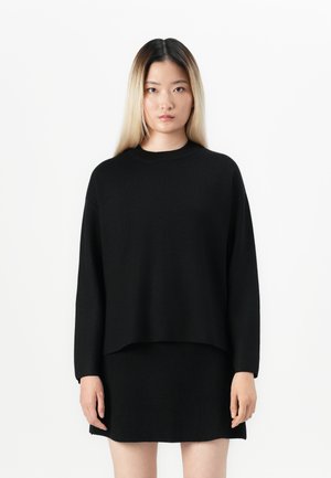 Black knit sweater with a round neck, dropped shoulders, and a loose fit, paired with a matching black knit skirt. Smooth texture.