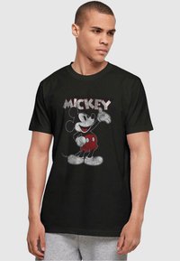 Camiseta de algodón negra con un gráfico de Mickey Mouse en pantalones cortos rojos. El diseño incluye el nombre "MICKEY" en letras estilizadas arriba.