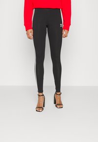 Zwarte leggings met witte zijstrepen, hoge taille, gemaakt van rekbaar materiaal, gecombineerd met zwarte hoge hakken sandalen.