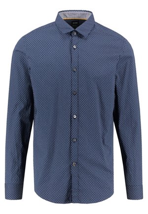 Chemise bleue à manches longues avec petit motif circulaire et col classique, présentée sur un fond blanc uni.