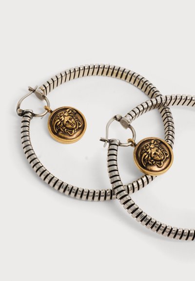 Boucles d'oreilles créoles en argent à texture rainurée, chacune ornée d'un petit pendentif rond en or embossé d'une tête de Méduse.