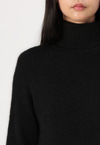 Black high-neck sweater made of textured knit fabric, featuring a ribbed pattern, long sleeves, and a relaxed fit.