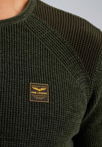 Maglione a maglia verde scuro con texture a coste e spalle lisce. Presenta una toppa con logo oro e nero con la scritta "PME LEGEND".