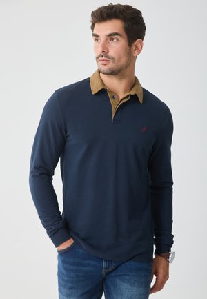 Langärmliges Poloshirt aus navyfarbigem Stoff mit einem kontrastierenden Kragen aus hellbraunem Cord. Auf der Brust befindet sich ein kleines gesticktes Logo.