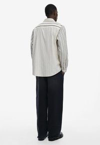 Camisa de rayas de manga larga en color crema y marino con un corte relajado y dobladillo redondeado. Combinada con pantalones de mezclilla oscuros de pierna ancha y zapatos negros.