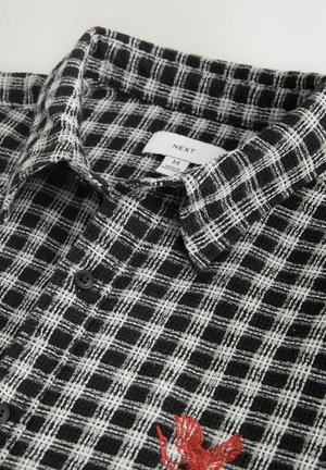 Fekete-fehér kockás ing texturált anyagból, patentos gallérral és piros hímzett díszítéssel. Méretcímke látható.