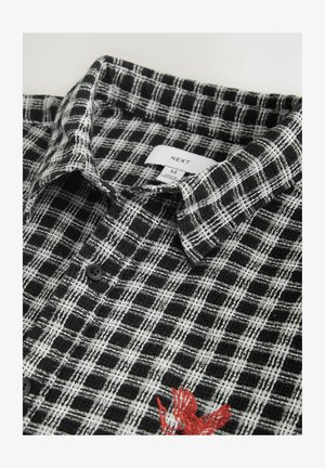 Fekete-fehér kockás ing texturált anyagból, patentos gallérral és piros hímzett díszítéssel. Méretcímke látható.