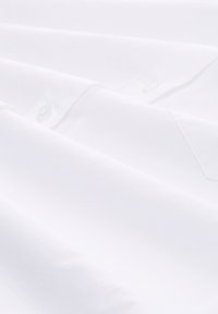 Bílá bavlněná košile s hladkou texturou, s límcem na knoflíky a jemným šitím podél lég a manžet.