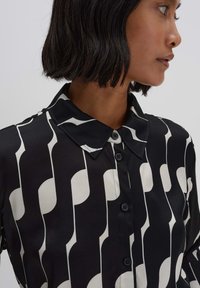 Camicia a righe bianche e nere con collo, dotata di chiusura a bottoni e una texture di tessuto liscia.