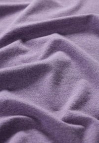 Violetti puuvillakangas, jossa on pehmeä rakenne, luonnollisia ryppyjä ja taitoksia, korostaen materiaalin joustavuutta ja laskeutuvuutta.
