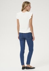 Haut blanc à volants à manches courtes, associé à un jean skinny bleu et des ballerines noires. Design simple avec une coupe décontractée. Texture lisse.