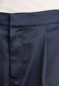 Námořnické modré kalhoty s hladkým materiálem, plochým předním dílem a neatně šitými detaily podél pásku a bočních švů.
